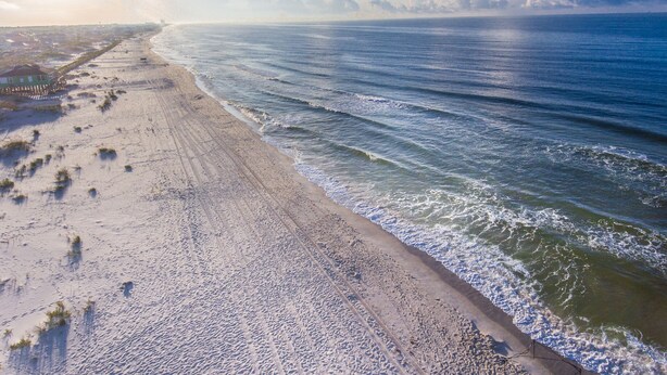 A beach with a wooden structure on the left and waves approaching the shore.