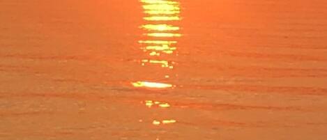 Un atardecer sobre un cuerpo de agua tranquilo, con un horizonte despejado.