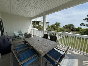 Portico coperto con tavolo in legno e sedie blu, affacciato su una zona residenziale con vista sull'oceano.