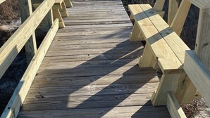 Een houten looppad dat naar een strand leidt, met bankjes aan beide zijden.