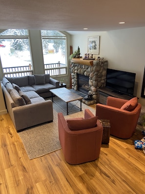 A living room with a stone fireplace, a large flat-screen TV, and a grey sectional sofa. - BEST LOCATION ON THE MOUNTAIN! Thunder Ridge 3 BR Ski in/Out Condo. Sleeps 8. (Fernie)