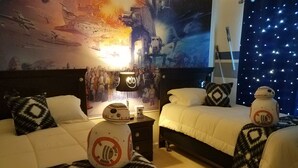 Un dormitorio con dos camas, cada una decorada con almohadas y un droide con temática de Star Wars. Un mural grande que representa una escena de batalla espacial adorna la pared detrás de las camas.