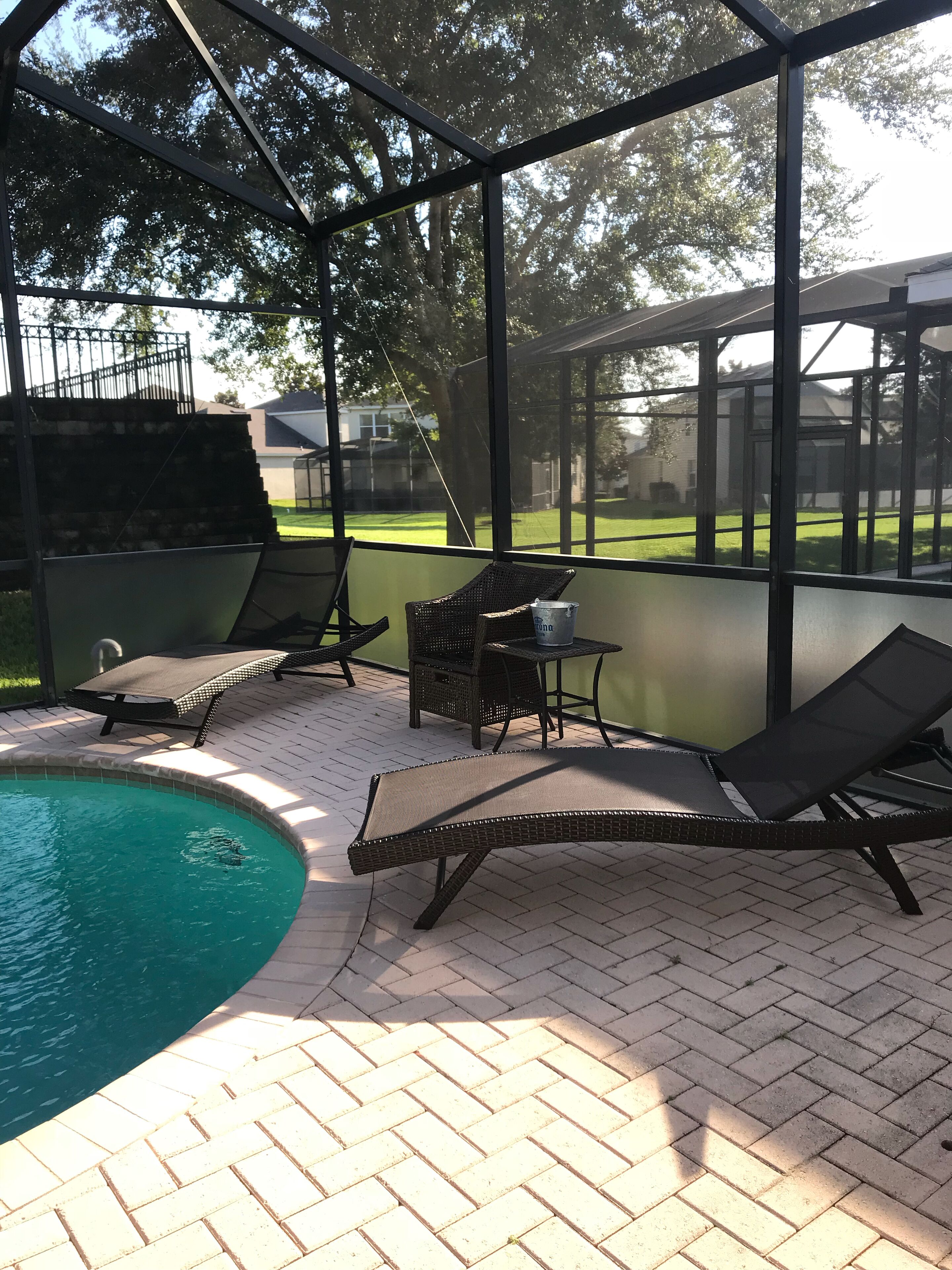 Un espacio al aire libre techado con piscina, sillas de descanso y una mesa con una bebida.
