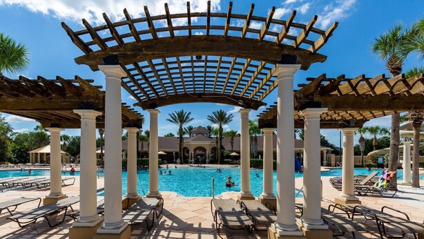 Un área de piscina con una pérgola, sillas de descanso y palmeras.