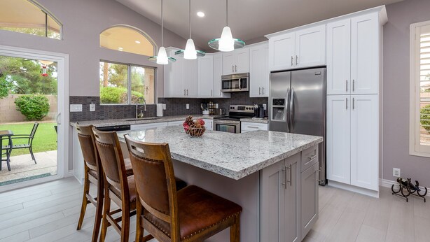 A modern kitchen with white cabinets, granite countertops, stainless steel appliances, and a central island with bar stools. - Sun, Fun, Golf, Swim, Relax in Your Own Resort Home. (Glendale)