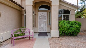 A house with a beige exterior, a decorative front door, a bench, and a well-maintained hedge. - Sun, Fun, Golf, Swim, Relax in Your Own Resort Home. (Glendale)