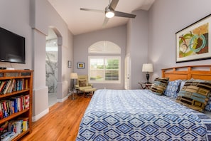 A bedroom with a bed, a bookshelf, a ceiling fan, a window with blinds, and a painting on the wall.