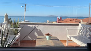 Un balcon avec vue sur la mer, des meubles blancs et une plante en pot.