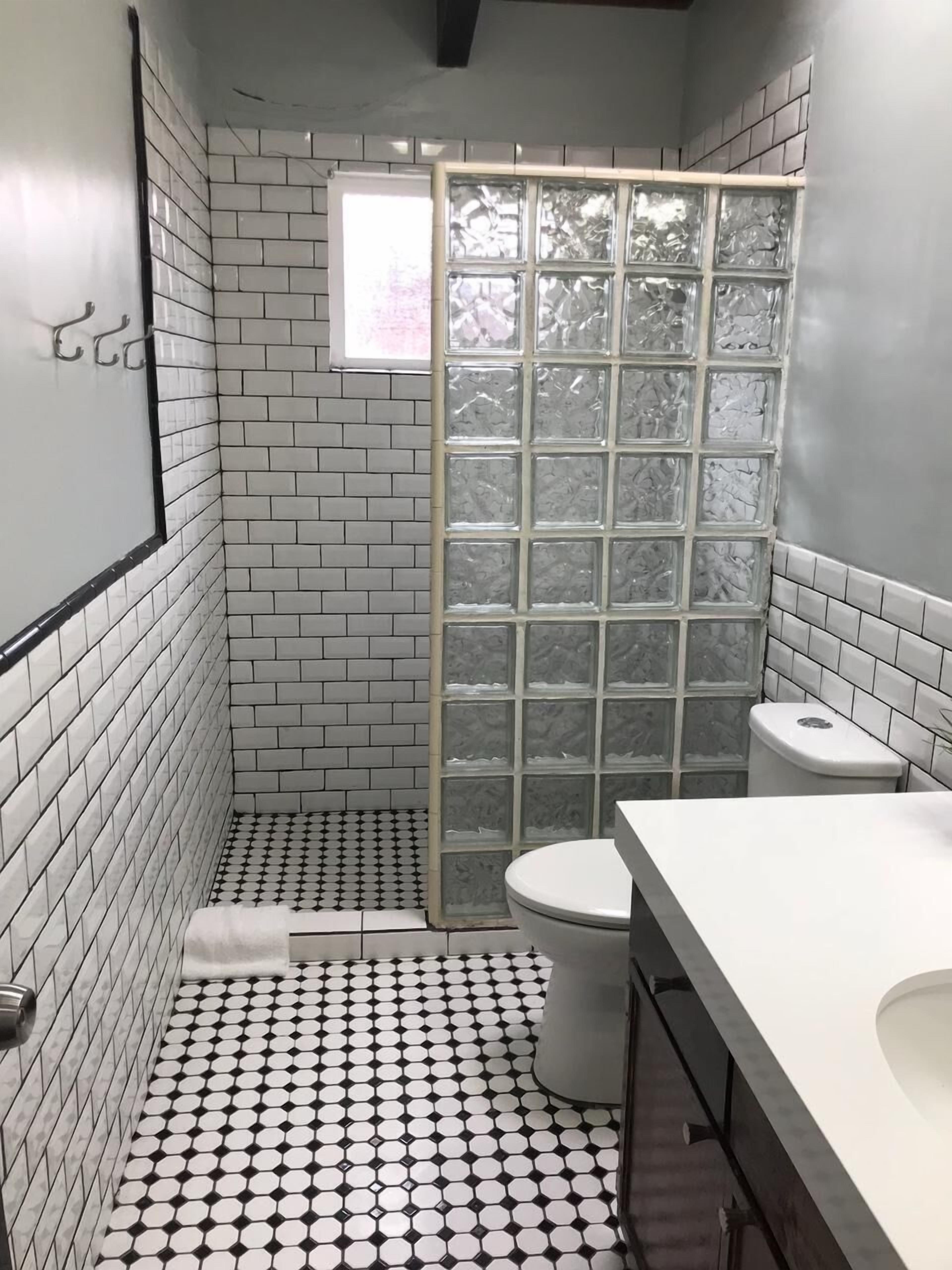 A bathroom with a white and black tiled floor, a white toilet, a white sink, and a shower with frosted glass panels.