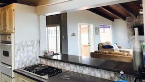 La cuisine est équipée d’une cuisinière à gaz, d’un four à micro-ondes et d’un plan de travail carrelé. Une fenêtre offre une vue sur l’extérieur.