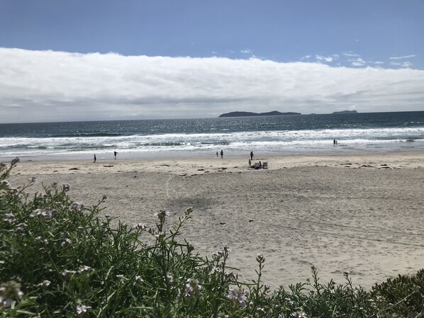Una playa con gente caminando por la orilla, un barco en el agua y unas islas a lo lejos.