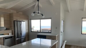 Una cocina moderna con una isla grande, electrodomésticos de acero inoxidable y vista al océano.