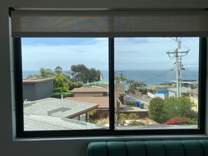 Enjoy a room with a large window offering a view of the coastal area, featuring a building with a tiled roof and a street with houses.