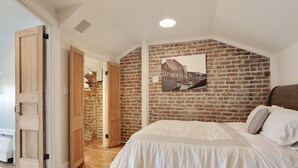 A bedroom with a brick wall, a bed with white bedding, and a wooden door. - Luxury 2-Story Condo / Prime Location (New Orleans)