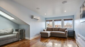 A room with a sectional sofa, a small table, and a built-in air conditioning unit. - Luxury 2-Story Condo / Prime Location (New Orleans)
