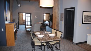 A dining area with a table set for six, chairs, a hanging light fixture, and a view into a living room.