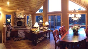 A cozy living room with a fireplace, a Christmas tree, and a dining area with wooden chairs and a table. - Luxury Home, Breathtaking Views, Hot Tub, Colorado Rocky Mountains (Estes Park)