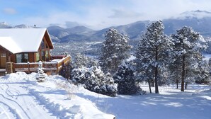 A wooden cabin with a snow-covered deck and a view of snow-covered trees and mountains. - Luxury Home, Breathtaking Views, Hot Tub, Colorado Rocky Mountains (Estes Park)
