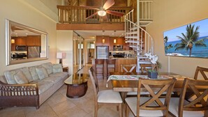 A spacious living area with a high ceiling, a dining table with chairs, a sofa, a coffee table, and a kitchen in the background.
