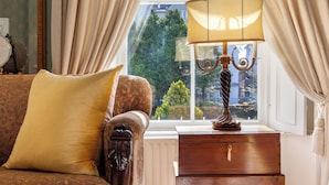 Une pièce avec un canapé, une lampe, une fenêtre avec des rideaux et une vue sur la verdure à l’extérieur.