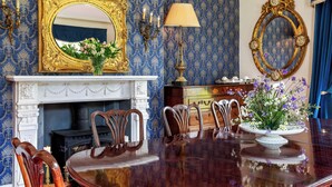 Une salle à manger avec une table en bois, des chaises, une cheminée et des miroirs décoratifs.