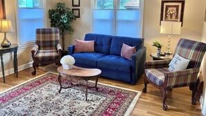 Un salon avec un canapé bleu, des fauteuils à carreaux, une table basse en bois et un tapis à motifs.