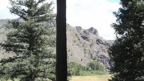 Ein Steinhaus mit Metall-Dach, mit Blick auf eine gebirgige Landschaft mit Bäumen.