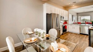 Una cocina moderna con armarios blancos, electrodomésticos de acero inoxidable y una zona de comedor con una mesa y sillas de vidrio.