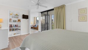 Une chambre à coucher comprenant un lit, une bibliothèque, un téléviseur et une porte-fenêtre coulissante donnant sur un balcon.
