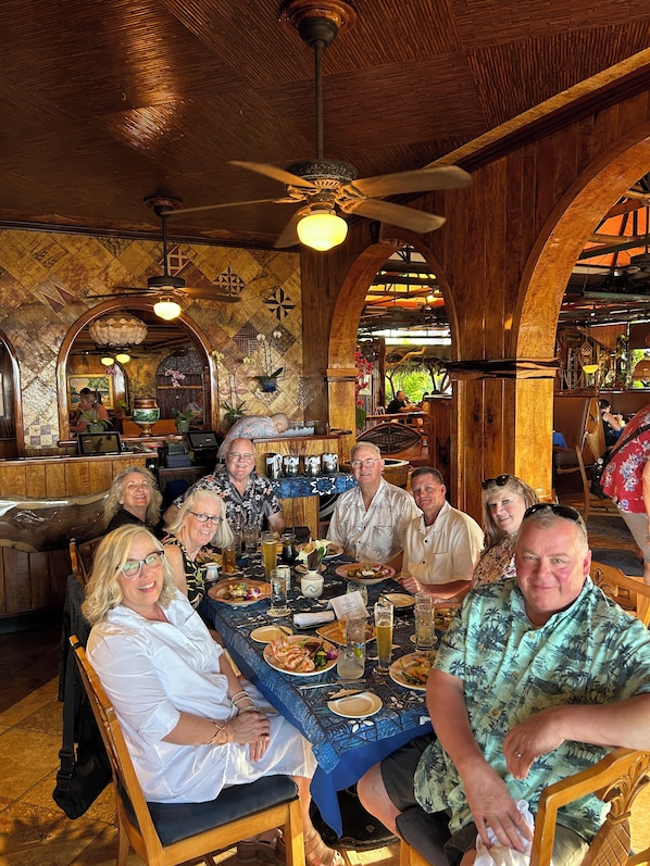 Um grupo de pessoas sentadas à mesa em um restaurante com arcos de madeira e um ventilador de teto.