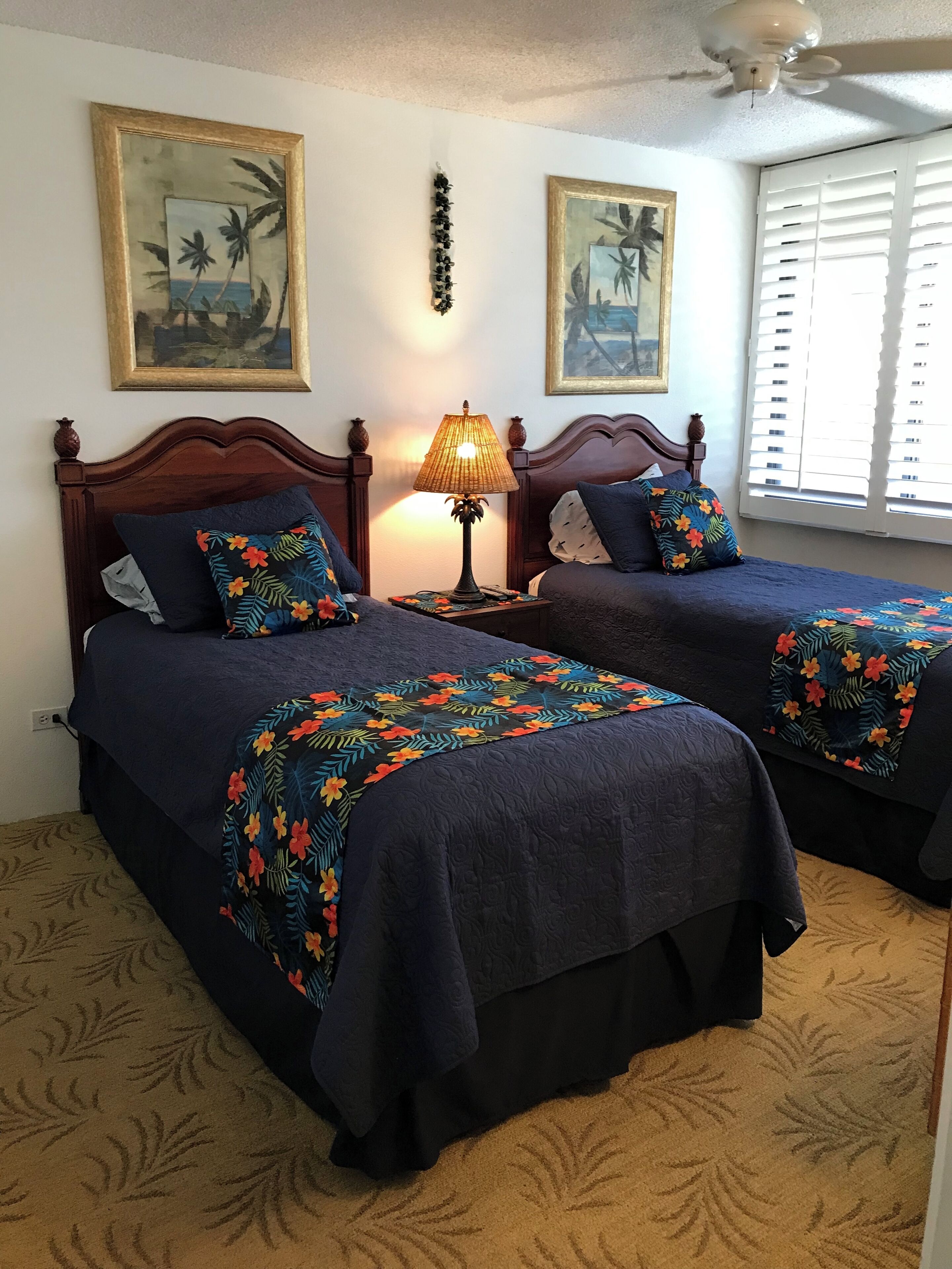 A bedroom with two beds, a nightstand with a lamp, and wall art.