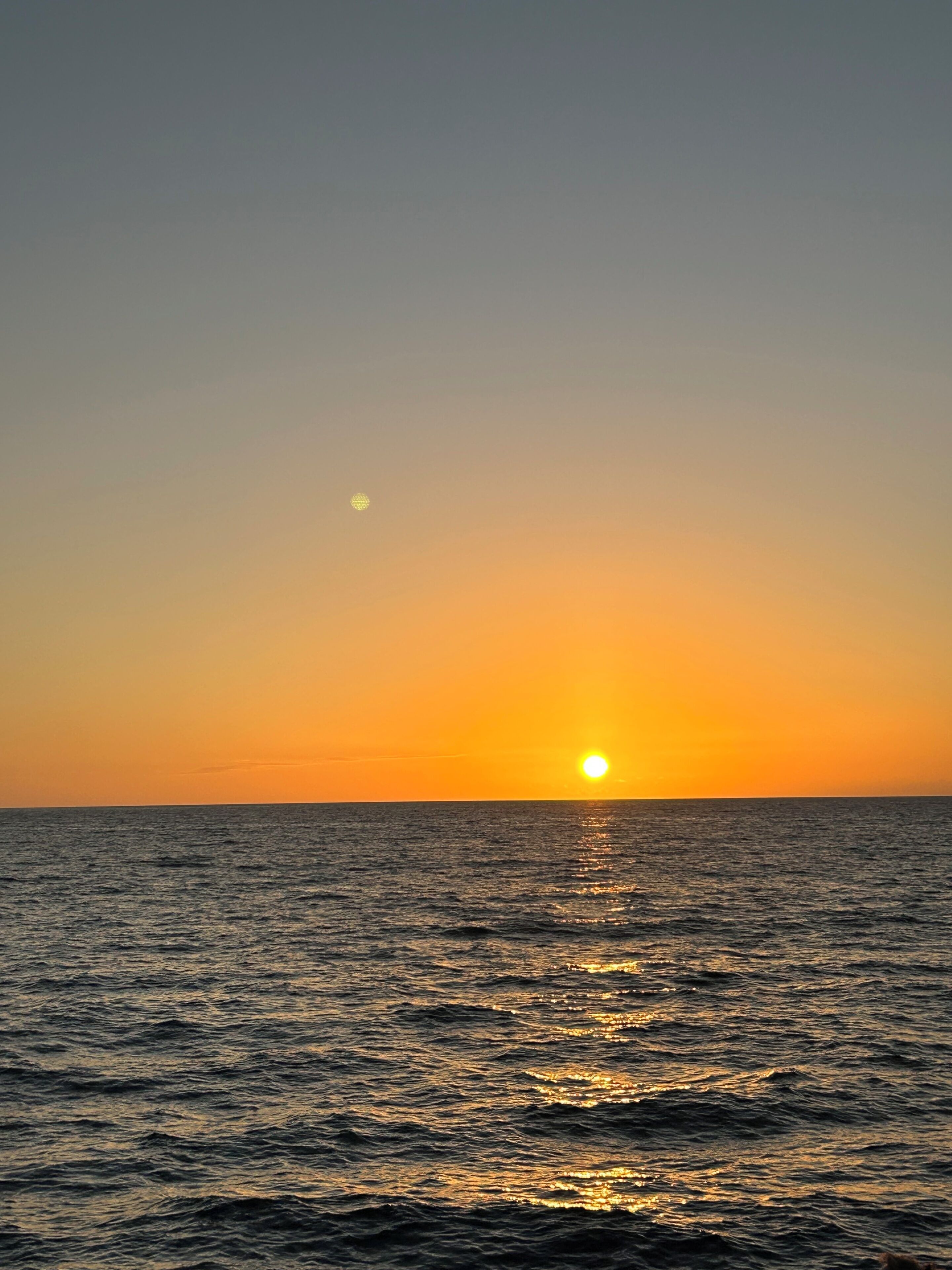 Een zonsondergang boven een rustige zee met een heldere horizon.