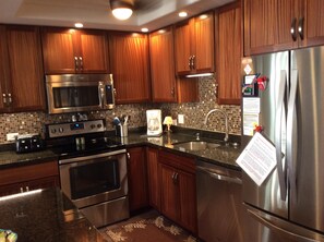 Enjoy cooking in this well-equipped kitchen with stainless steel appliances, wooden cabinetry, and a granite countertop.