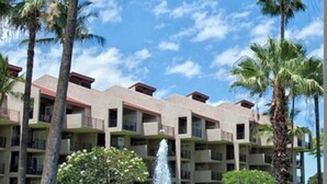 A multi-story hotel with a central courtyard featuring a fountain, surrounded by palm trees and greenery.