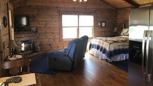 A cozy cabin with a wooden interior, a fireplace, a television, a bed, and a refrigerator. - Couples Getaway with a Great Mountain View (Blue Ridge)