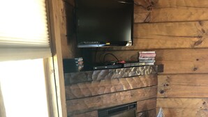 A wooden interior with a fireplace, a television mounted above it, and a window to the left. - Couples Getaway with a Great Mountain View (Blue Ridge)