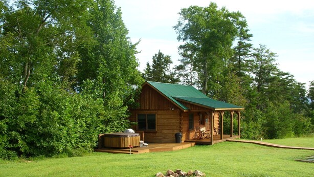 A wooden cabin with a green roof, a hot tub, and a covered porch with chairs. - Couples Getaway with a Great Mountain View (Blue Ridge)