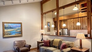 Una sala de estar acogedora con un ventanal grande, un sillón de cuero, un sofá, una mesa de centro y un tapete estampado.