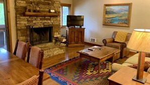 Una sala de estar acogedora con chimenea de piedra, un televisor y un cuadro en la pared.