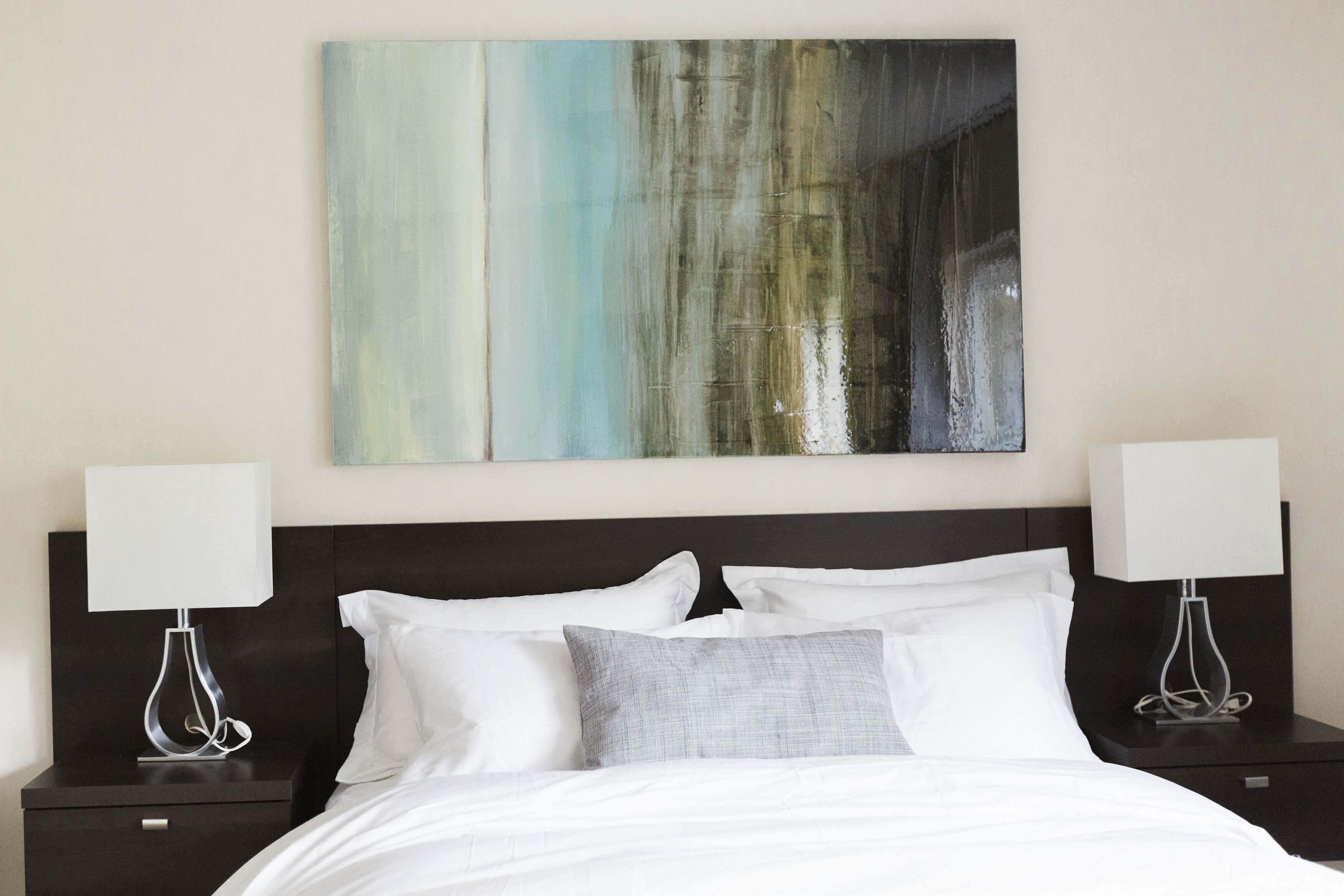 Une chambre d’hôtel moderne avec un grand lit, deux tables de chevet avec des lampes et un grand tableau abstrait accroché au mur.