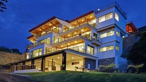 Une maison moderne à plusieurs étages, dotée d’un toit plat, de grandes fenêtres et d’un balcon situé aux étages supérieurs.