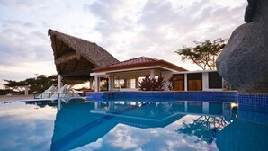 Ein Resort mit Swimmingpool, einem strohgedeckten Gebäude und einer großen Felsformation.