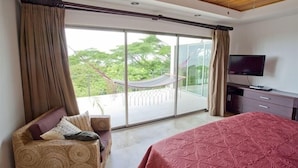 Une chambre avec un grand lit, une télévision, un canapé et une vue sur un balcon agrémenté d’un hamac.