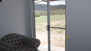 A room with a plaid sofa, a sliding glass door leading to a grassy outdoor area, and a yellow tag on the door handle. - Donegal Farmstay (Sandy Flat)