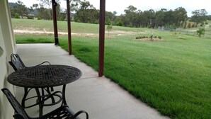 A covered patio with a table and chairs, overlooking a well-maintained lawn and trees. - Donegal Farmstay (Sandy Flat)