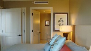 Une chambre à coucher avec un lit, des oreillers, une table de chevet avec une lampe, une porte et un tableau encadré au mur.
