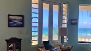 A room with a desk, laptop, and chair, a lamp, and a view of the ocean through large windows. - On Ocean&Sandy Beach-Private access to beach! Air conditioned. Standby Generator (Rincon)