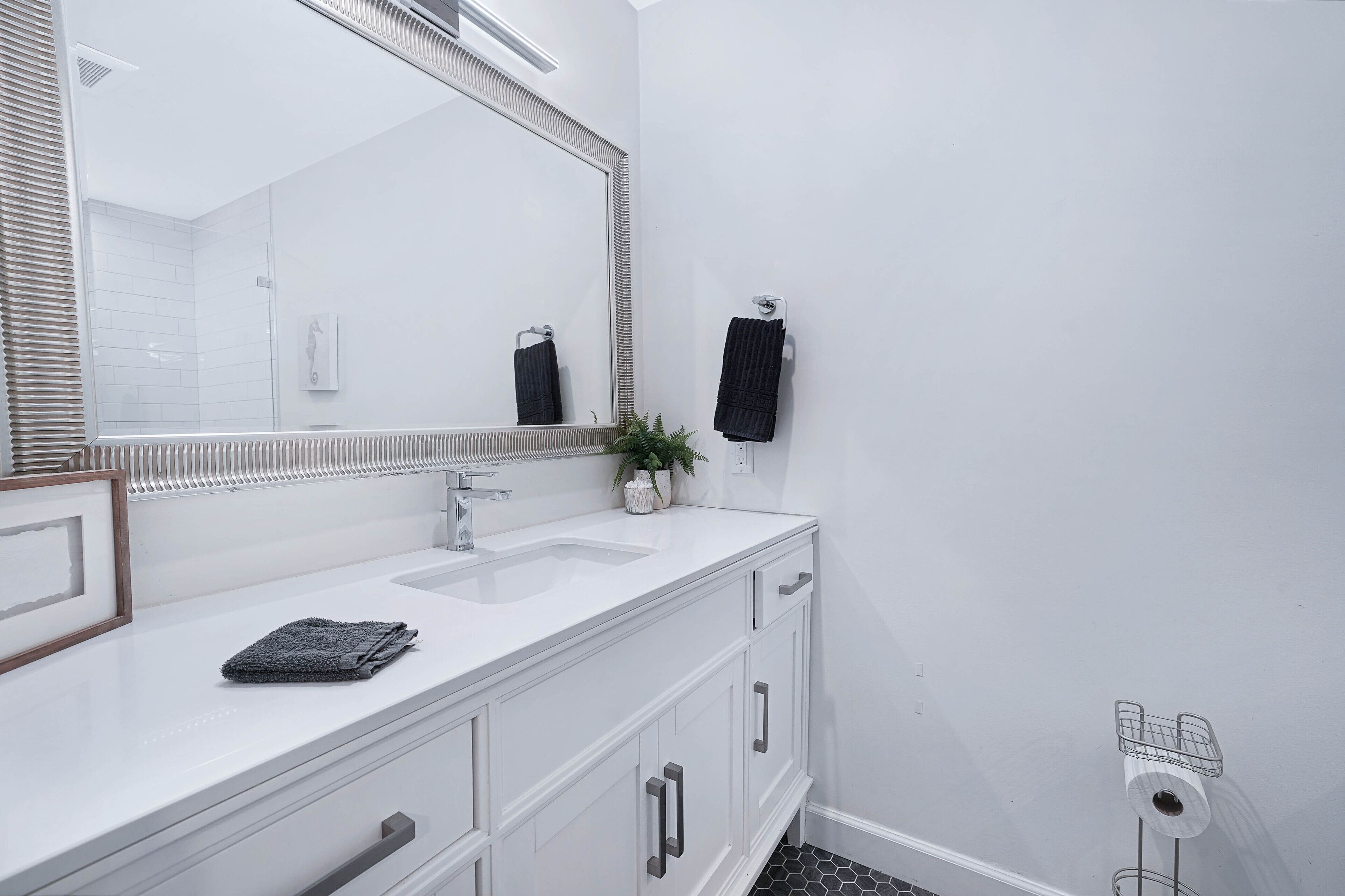A bathroom with a white vanity, a large mirror, and a towel rack.