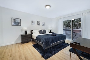 Ein modernes Schlafzimmer mit Bett, Nachttischen, einem Schreibtisch und einem Balkon mit Gartenmöbeln.
