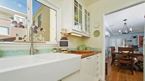 A kitchen with a large white sink, white cabinets, a wooden countertop, and a dining area with wooden chairs and a table. - A PERFECT BEACH COTTAGE  Exclusive Private Retreat - STEPS TO BEACH AND BAY (San Diego)